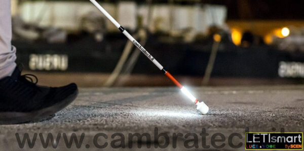 Immagine del LETIsmart Luce, in funzione, quindi illuminato, applicato ad un bastone usato di notte in città da una persona che sta camminando, immagine usata anche per rappresentare la categoria luci e voci per bastoni